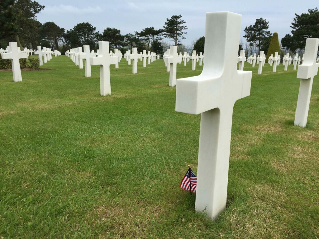 Croix blanche avec petit drapeau américain au pied, dans le cimetière militaire de Normandie